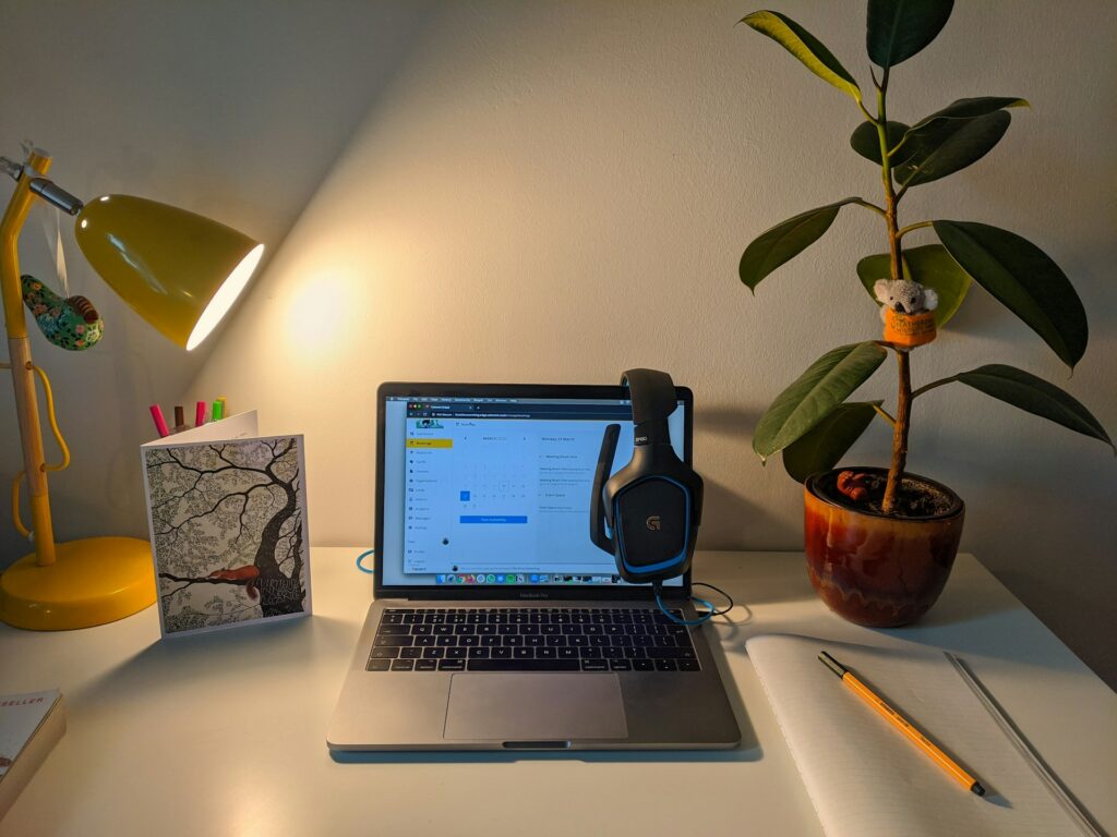 Bureau dans une maison avec un ordinateur portable et une lampe de bureau allumés, un casque est posé sur l'ordinateur. Cette image illustre une scène de télétravail en lien avec le sujet de notre article : un accident au domicile peut-il être reconnu comme accident du travail ?